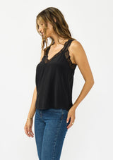 [Color: Black] A side facing image of a brunette model wearing our beloved lace trim camisole, now reimagined with elegant lace-trimmed straps and a sophisticated lace V-neckline. This versatile piece features a flattering racerback design with delicate pretty lace straps, making it the perfect layering essential.