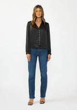 [Color: Black] A front facing image of a brunette model wearing a black satin blouse with a collar, v-neckline, button front, and long sleeves. Styled with with blue denim jeans. 