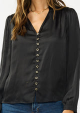 [Color: Black] A detail image of a brunette model wearing a black satin blouse with a collar, v-neckline, button front, and long sleeves. 