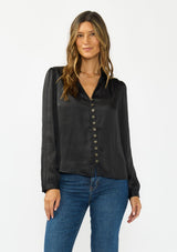 [Color: Black] A front facing image of a brunette model wearing a black satin blouse with a collar, v-neckline, button front, and long sleeves. 