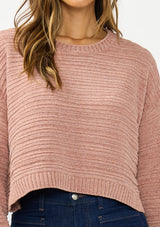 [Color: Rose] A detail image of a brunette model wearing a dusty pink chenille sweater with a round neck and long sleeves with dropped shoulders. Styled with a dark wash denim with patch pockets.