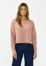 [Color: Rose] A front facing image of a brunette model wearing a dusty pink chenille sweater with a round neck and long sleeves with dropped shoulders. Styled with a dark wash denim with patch pockets.