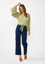 [Color: Olive/Rose] A front facing image of a brunette model wearing a green bohemian floral top with wide sleeves, a v neckline,  a button front, and a tie front detail. Styles with a dark wash denim with patch pockets. 