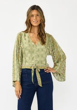 [Color: Olive/Rose] A front facing image of a brunette model wearing a green bohemian floral top with wide sleeves, a v neckline,  a button front, and a tie front detail. Styles with a dark wash denim with patch pockets. 