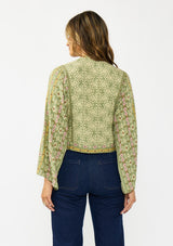 [Color: Olive/Rose] A back facing image of a brunette model wearing a green bohemian floral top with wide sleeves, a v neckline,  a button front, and a tie front detail. Styles with a dark wash denim with patch pockets. 