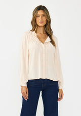 [Color: Petal] A front facing image of a brunette model wearing a light pink blouse with embroidered lace, a button front, and long flowy sleeves. Styled with a dark wash denim with patch pockets. 