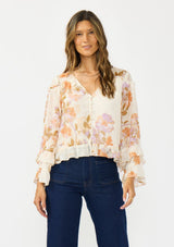 [Color: Ivory/Rust] A front facing image of a brunette model wearing an ivory and orange floral blouse with a v neckline, button front, long sleeves, and ruffle details. 