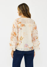 [Color: Ivory/Rust] A back facing image of a brunette model wearing an ivory and orange floral blouse with a v neckline, button front, long sleeves, and ruffle details. 