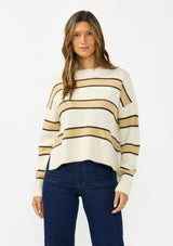 [Color: Oatmeal] A front facing image of a brunette model wearing a beige and yellow striped pullover sweater with a crew neckline, side vents, and dropped shoulders. Styled with a dark wash denim with patch pockets. 