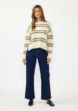 [Color: Oatmeal] A front facing image of a brunette model wearing a beige and yellow striped pullover sweater with a crew neckline, side vents, and dropped shoulders. Styled with a dark wash denim with patch pockets and black loafers. 