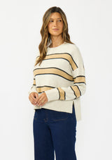 [Color: Oatmeal] A side facing image of a brunette model wearing a beige and yellow striped pullover sweater with a crew neckline, side vents, and dropped shoulders. Styled with a dark wash denim with patch pockets and black loafers. 