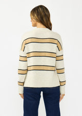 [Color: Oatmeal] A back facing image of a brunette model wearing a beige and yellow striped pullover sweater with a crew neckline, side vents, and dropped shoulders. Styled with a dark wash denim with patch pockets and black loafers. 