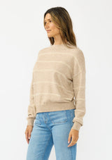 [Color: Heather Taupe] A side facing image of a brunette model wearing a brown striped pullover sweater with a striped design and a high neckline. 