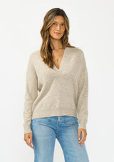 [Color: Heather Cement] A front facing image of a brunette model wearing a beige pullover sweater with a v neckline long sleeves with dropped shoulders. Styles with light wash denim with patch pockets. 