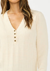 [Color: Peach] A detail image f a brunette model wearing a cream fuzzy pullover sweater with a v neckline, button front, and long sleeves. 