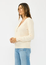 [Color: Peach] A side facing image f a brunette model wearing a cream fuzzy pullover sweater with a v neckline, button front, and long sleeves. 