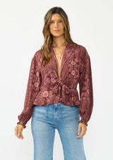 [Color: Wine/Dusty Rose] A front facing image of a brunette model wearing a bohemian burgundy floral tie front top with a deep v neckline and long sleeves. 