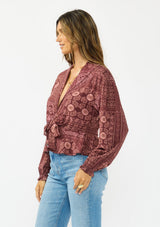 [Color: Wine/Dusty Rose] A side facing image of a brunette model wearing a bohemian burgundy floral tie front top with a deep v neckline and long sleeves. 