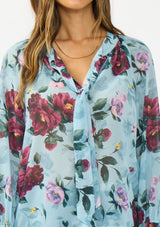 [Color: Blue/Burgundy] A detail image of a brunette model wearing a blue and burgundy floral blouse with a tie neck detail and button front. 