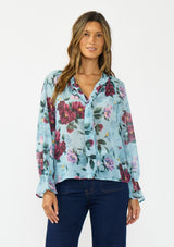 [Color: Blue/Burgundy] A front facing image of a brunette model wearing a blue and burgundy floral blouse with a tie neck detail and button front. Styled with dark wash denim. 