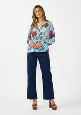 [Color: Blue/Burgundy] A front facing image of a brunette model wearing a blue and burgundy floral blouse with a tie neck detail and button front. Styled with dark wash denim and brown platform heels.