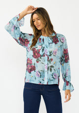 [Color: Blue/Burgundy] A front facing image of a brunette model wearing a blue and burgundy floral blouse with a tie neck detail and button front. Styled with dark wash denim. 