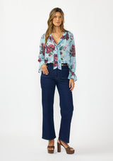 [Color: Blue/Burgundy] A front facing image of a brunette model wearing a blue and burgundy floral blouse with a tie neck detail and button front. Styled with dark wash denim and brown platform heels. 