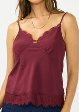 [Color: Merlot] A detail image image of a brunette model wearing a burgundy lace cami with spaghetti straps. Styled with dark wash denim. 