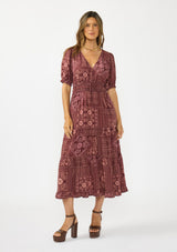 [Color: Wine/Dusty Rose] A front facing image of a brunette model wearing a burgundy bohemian midi dress with  short puff sleeves, a v neckline, elastic waist, and a tiered skirt with ruffle trim. Styled with brown block heels. 