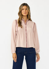 [Color: Mauve] A front facing image of a brunette model wearing a pink bohemian blouse with embroidery, a button front, and pintuck detailing. Styled with a dark wash denim with patch pockets. 