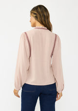 [Color: Mauve] A back facing image of a brunette model wearing a pink bohemian blouse with embroidery, a button front, and pintuck detailing. Styled with a dark wash denim with patch pockets. 