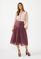 [Color: Plum] A front facing image of a model wearing an embroidered blouse with a crinkled purple midi skirt with pleats. 