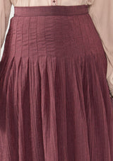 [Color: Plum] A front facing image of a model wearing a crinkled purple midi skirt with pleats. 