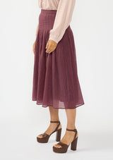 [Color: Plum] A side facing image of a model wearing a crinkled purple midi skirt with pleats. 