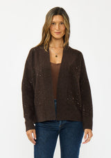 [Color: Brown] A front facing image of a brunette model wearing a brown open front cardigan with sequins and rib trims. 