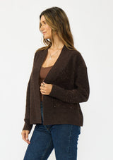 [Color: Brown] A side facing image of a brunette model wearing a brown open front cardigan with sequins and rib trims. 