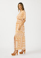 [Color: Taupe/Natural] A side facing image of a brunette model wearing a brown floral bohemian maxi dress with short dolman sleeves, a v neckline, smocked waist, and a front slit. 