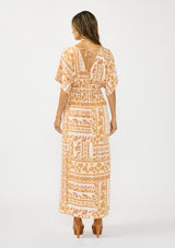 [Color: Taupe/Natural] A back facing image of a brunette model wearing a brown floral bohemian maxi dress with short dolman sleeves, a v neckline, smocked waist, and a front slit. 