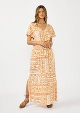 [Color: Taupe/Natural] A front facing image of a brunette model wearing a brown floral bohemian maxi skirt with a smocked waist and side slits. Styled with a matching brown floral tie front top. 