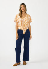 [Color: Taupe/Natural] A front facing image of a brunette model wearing a bohemian brown floral top with a v neckline, short sleeves, and a tie front detail.