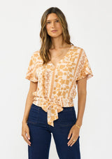 [Color: Taupe/Natural] A front facing image of a brunette model wearing a bohemian brown floral top with a v neckline, short sleeves, and a tie front detail.