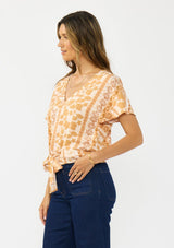 [Color: Taupe/Natural] A side facing image of a brunette model wearing a bohemian brown floral top with a v neckline, short sleeves, and a tie front detail.