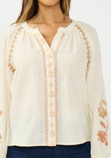 [Color: Natural] A detail image of a brunette model wearing an embroidered blouse with a hidden button front. 