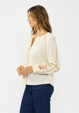[Color: Natural] A side facing image of a brunette model wearing an embroidered blouse with a hidden button front. 