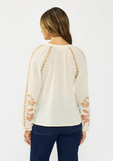 [Color: Natural] A back facing image of a brunette model wearing an embroidered blouse with a hidden button front. 