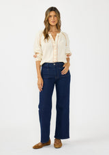 [Color: Natural] A front facing image of a brunette model wearing an embroidered blouse with a hidden button front. Styled with a dark wash denim with patch pockets.