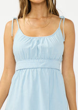 [Color: Light Denim Blue] A detail image of a brunette model wearing a light blue cotton midi dress with tie shoulders,