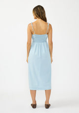 [Color: Light Denim Blue] A back facing image of a brunette model wearing a light blue cotton midi dress with tie shoulders and styled with brown suede flats. 