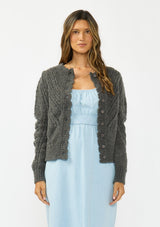 [Color: Charcoal] A front facing image of a brunette model wearing a grey pointelle knit button front cardigan with a round neckline and long puff sleeves. 