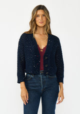 [Color: Navy] A front facing image of a brunette model wearing a navy cropped knit cardigan with sequins and a button front. 